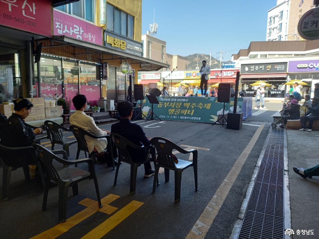 간이 무대가 설치되어 있고 그곳에서 동부시장 맥주축제 앵콜파티 행사가 진행되고 있으며 앞에 놓인 의자에 사람들이 앉아서 행사를 구경하고 있다.