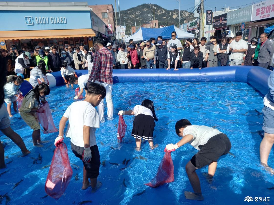 대형 풍선 수조 안에 물과 물고기가 담겨있고 어린이들이 들어가서 맨손으로 물고기 잡기 체험을 하고 있는 모습