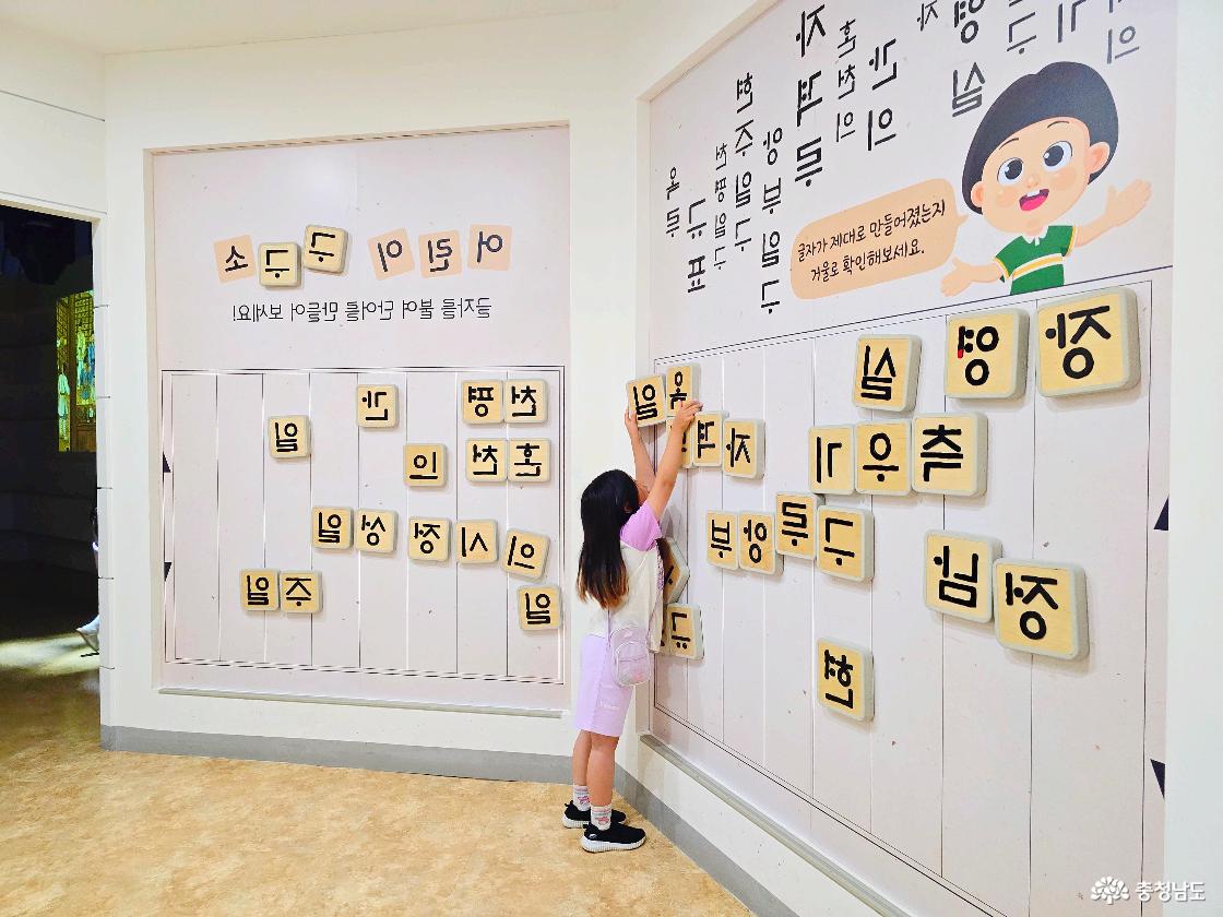 장영실과학관 실내 체험존에서 아이가 벽면에 붙은 한글 자석 블록을 옮기며 글자를 맞춰보는 언어 놀이 체험 모습입니다.